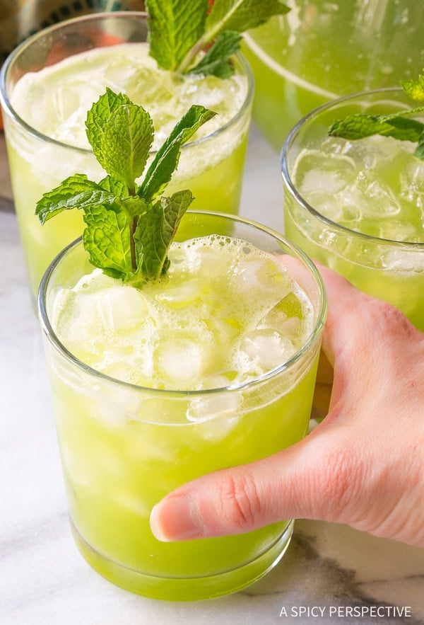 Three glasses of cucumber agua fresca with a hand grabbing one glass. 