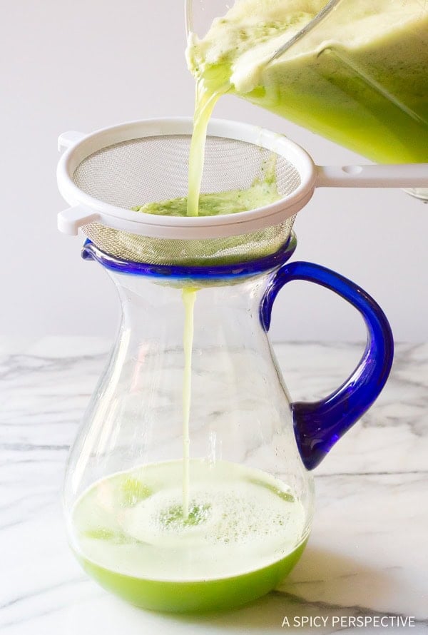 Hand pouring the agua fresca from the blender into a pitcher with a strainer on top. 