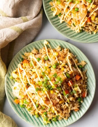Top down view of a green plate piled with shrimp fried rice, topped with a zig zag drizzle of yum yum sauce.
