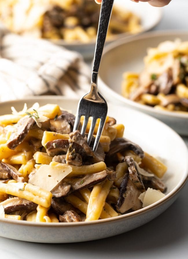 fork taking a bite of mushrooms from the bowl of noodles and parmesan