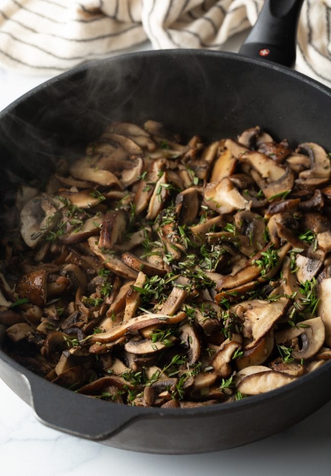 mushrooms sauteed in a skillet with fresh herbs and cooking sherry