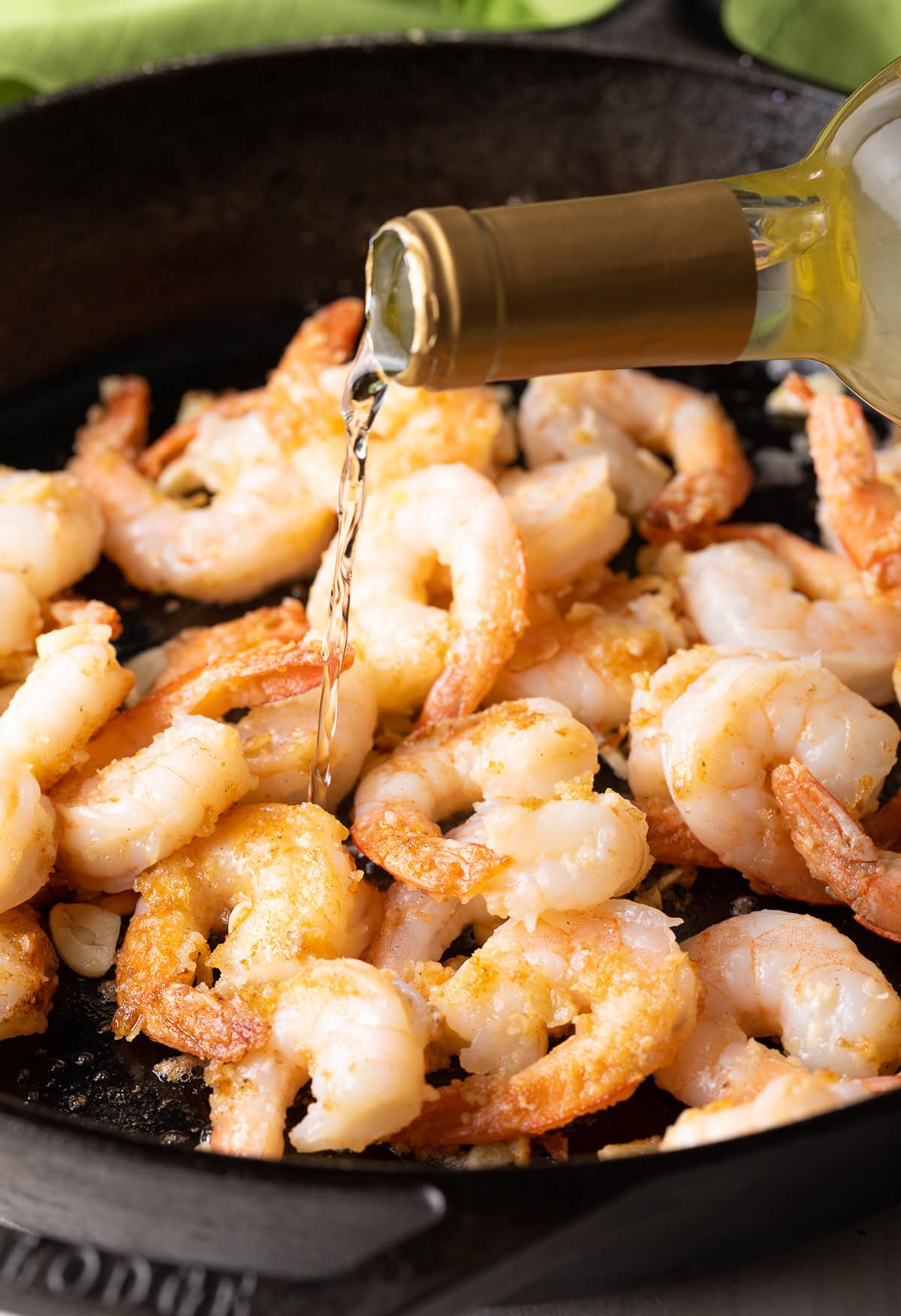 Shrimp being cooked in a cast iron skillet with wine being poured into the pan. 