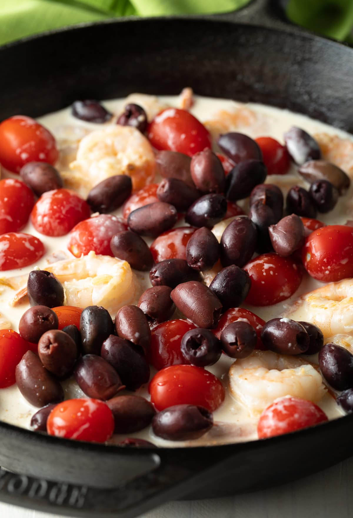 Shrimp cooking with tomatoes and olives in a cast iron skillet. 