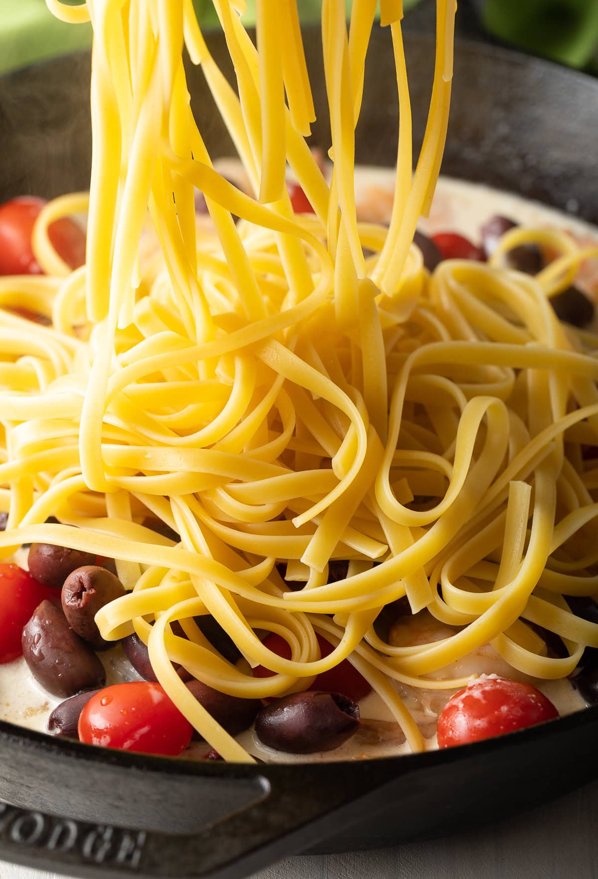 Noodles being added to the white wine sauce in a pan. 