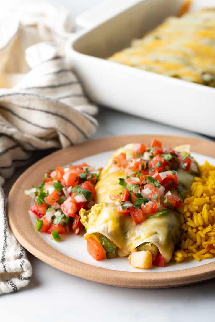 White plate with serving of pico de gallo, two chicken enchiladas with green sauce and pico de gallo, and spanish rice.