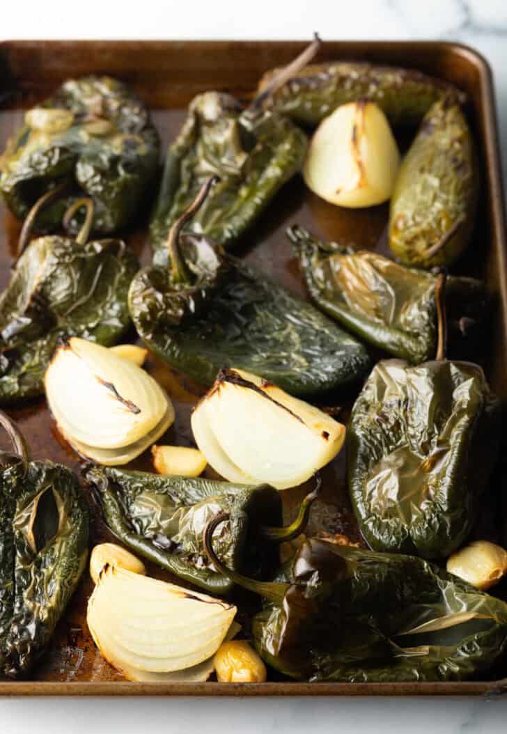 Roasted poblano peppers and chunks of onion, cloves of garlic on a baking sheet.