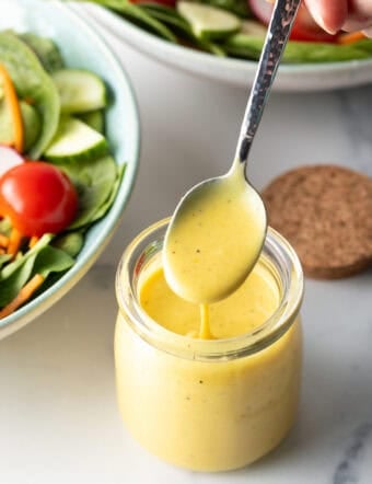 Metal spoon over a jar of honey mustard dressing, showing a serving to camera.
