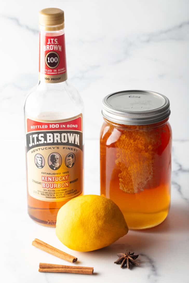 Recipe ingredients together: large mason jar of honey, whole lemon, and bottle of bourbon.