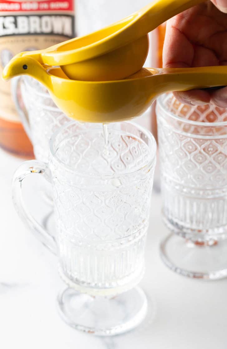 Use a yellow juicer to juice a lemon over a clear mug with handle.