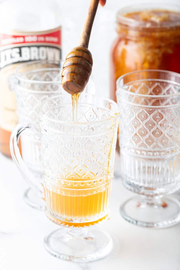 Adding honey to a clear handled mug.