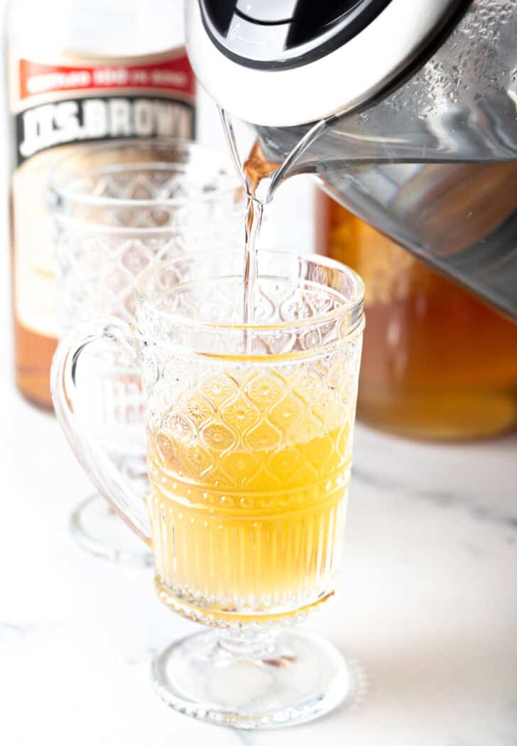 Pouring tea from a metal kettle into a clear glass mug.