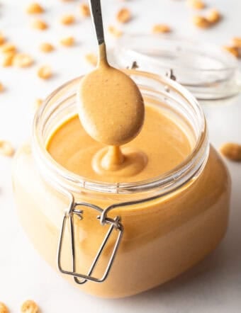A spoon taking a scoop of peanut butter from a glass jar, showing the butter to camera.