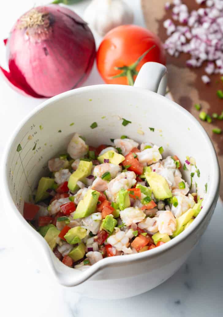 White bowl with a combination of shrimp, and chopped avocado, green and red peppers, and cilantro.
