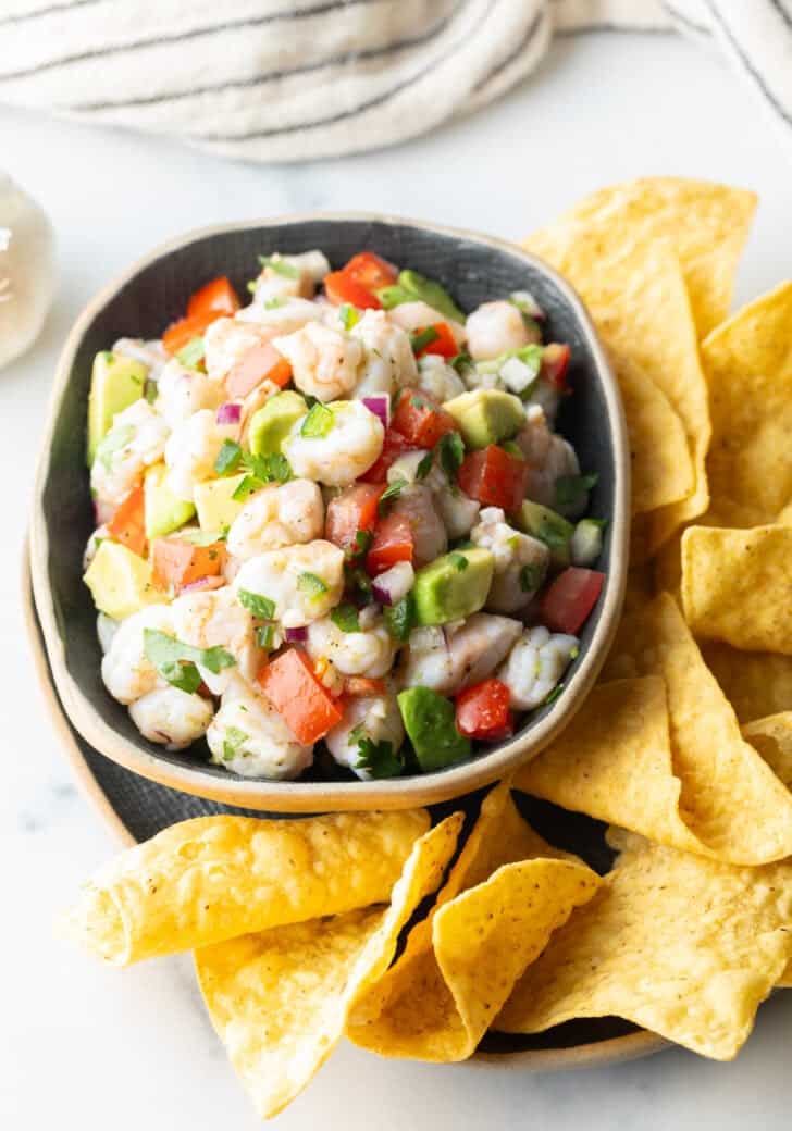 Top down view yellow bowl with shrimp ceviche. The bowl is surrounded by tortilla chips.