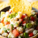 Yellow bowl of shrimp ceviche with a tortilla chip sticking in the middle.