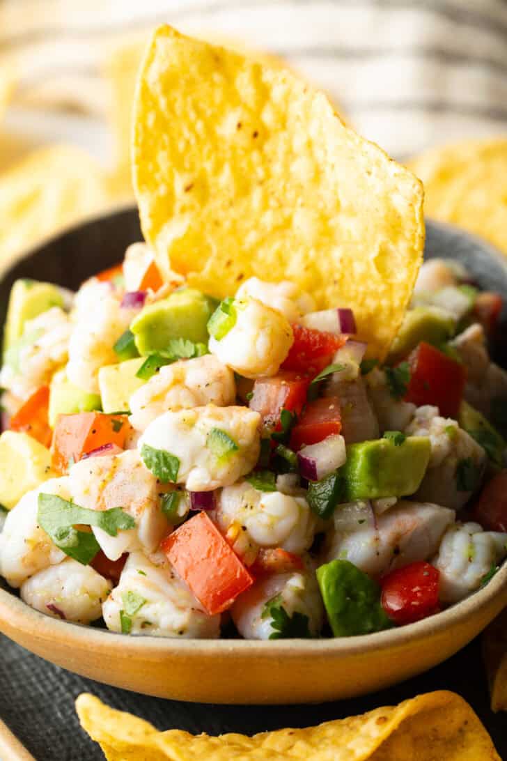 Yellow bowl of shrimp ceviche with a tortilla chip sticking in the middle.