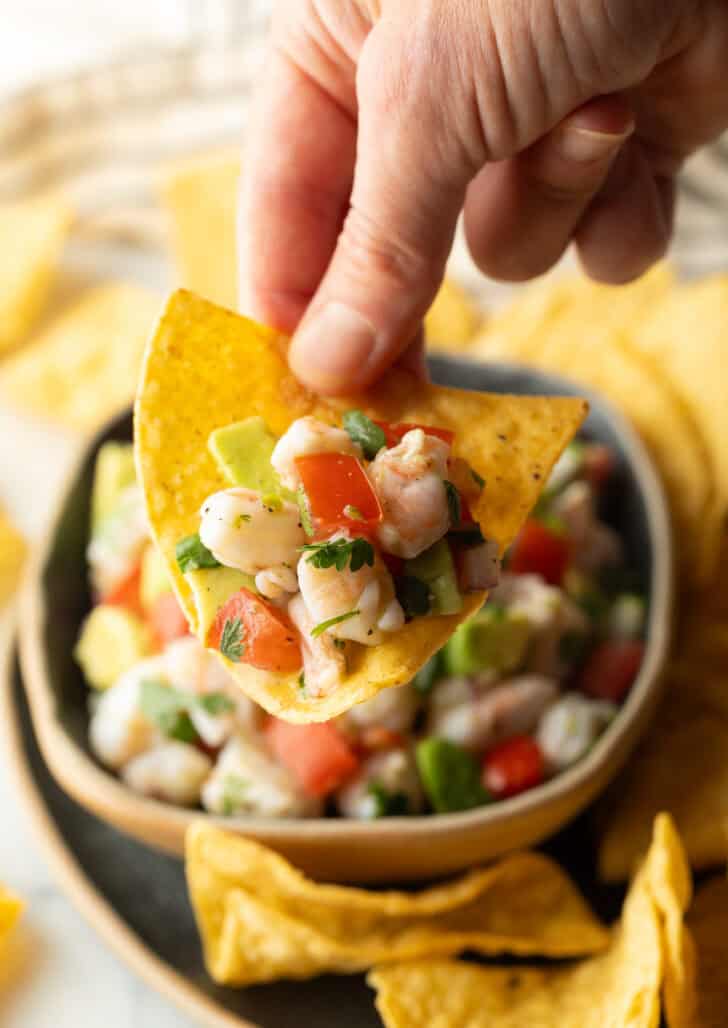 How to Make Shrimp Ceviche - Hand showing a scoop of ceviche on a tortilla chips held to camera.