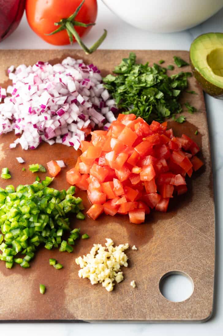 Recipe ingredients: Piles of chopped red peppers, green peppers, garlic, red onion, and cilantro.