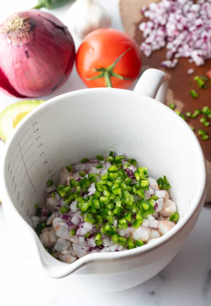 White bowl with raw shrimp and peppers on top.