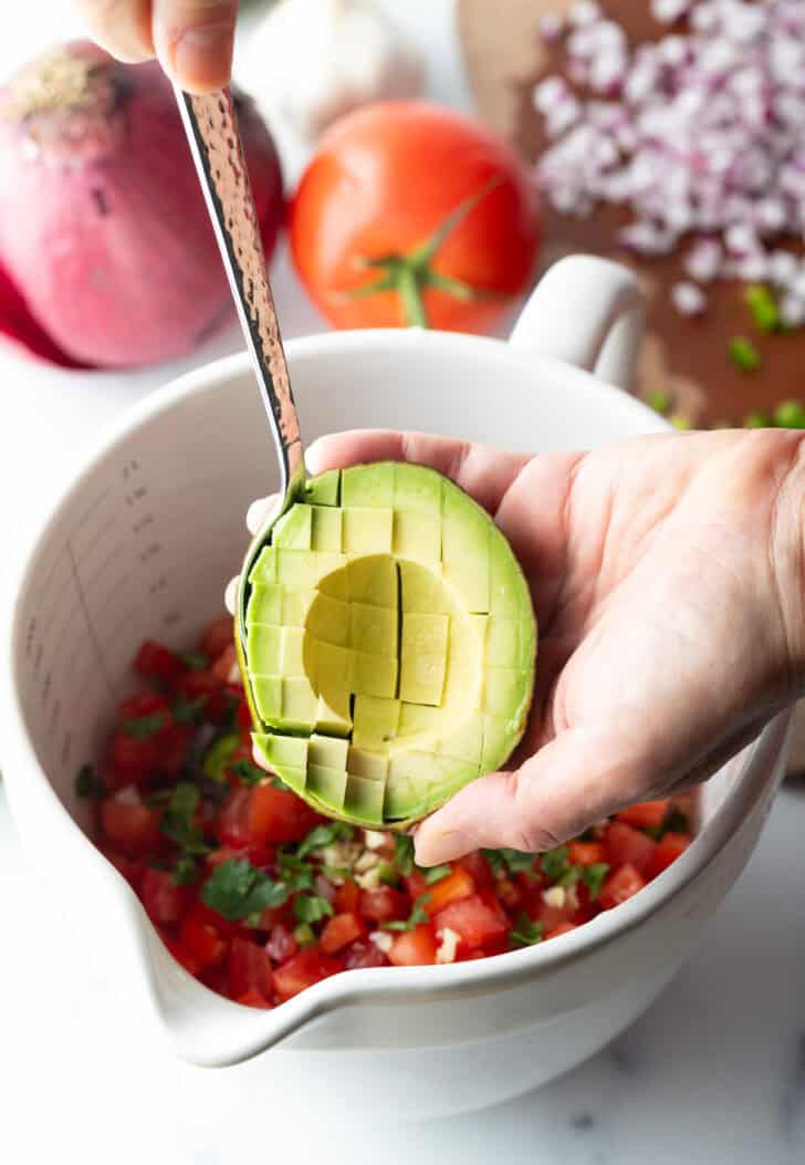 Hand showing how to slice half of an avocado with a sharp knife.