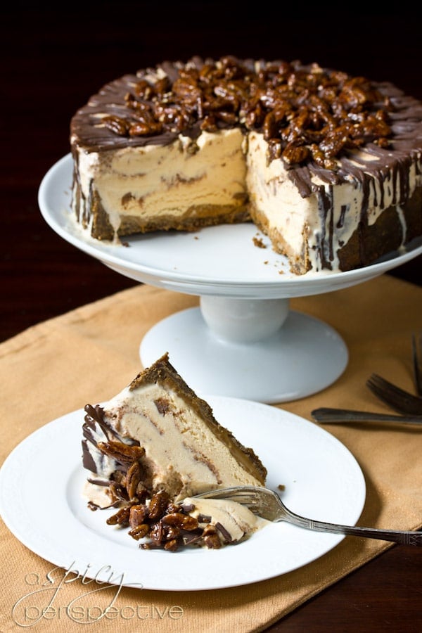Slice of ice cream cake on a plate with the cake in the background on a cake stand. 