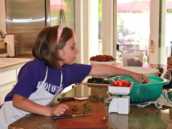 Girl next to a kitchen counter chopping strawberries. 