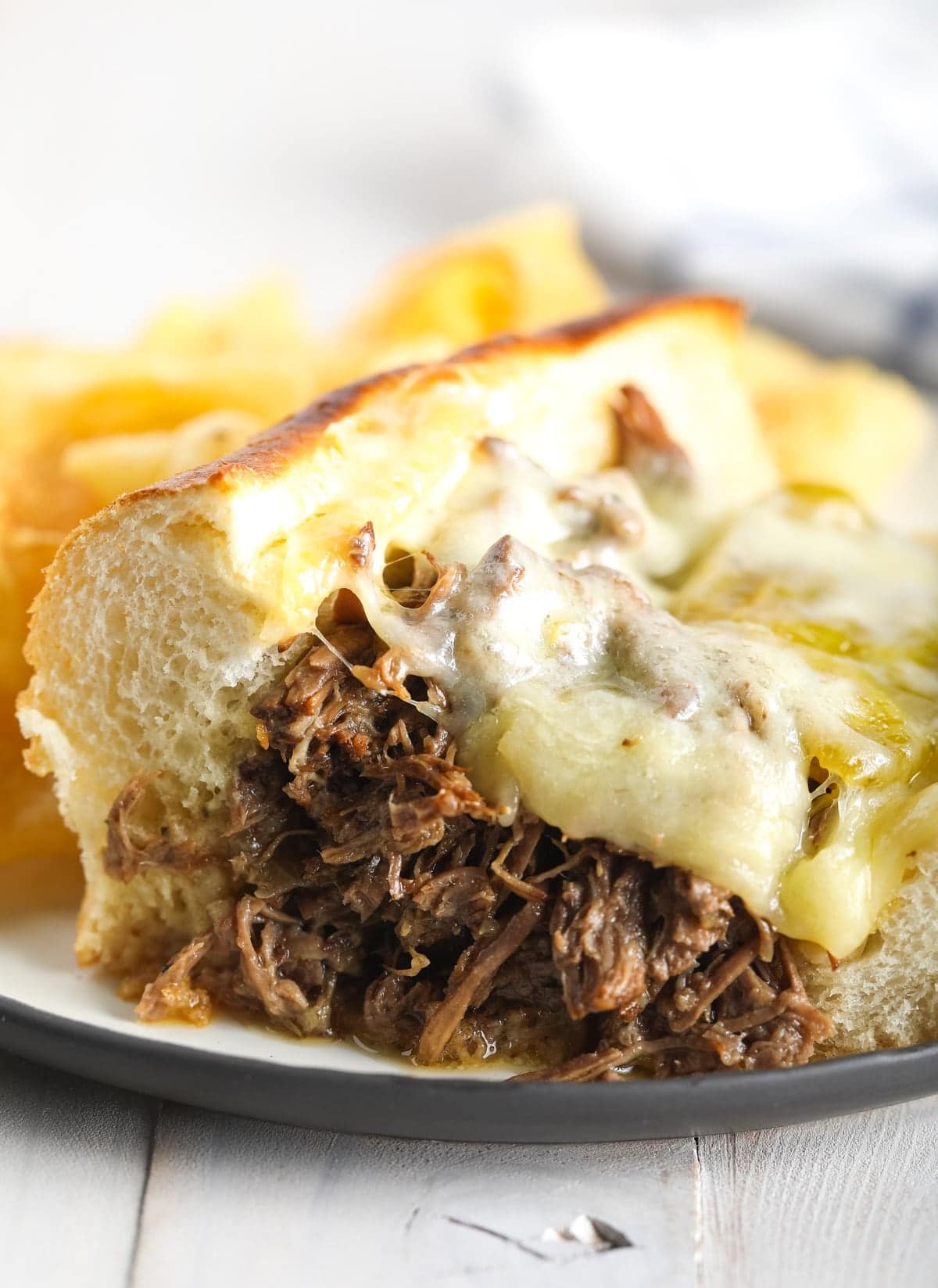 Shredded Italian beef sandwich with melted cheese on top, served on a plate. 
