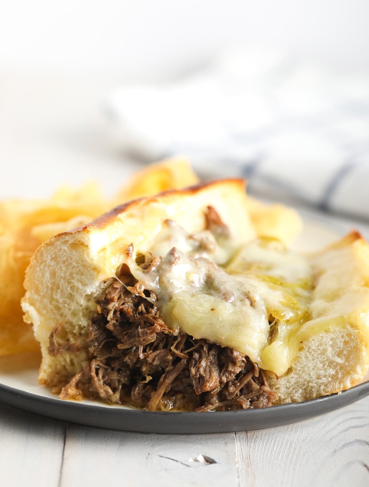Italian beef sandwich with melted cheese on top on a plate. 
