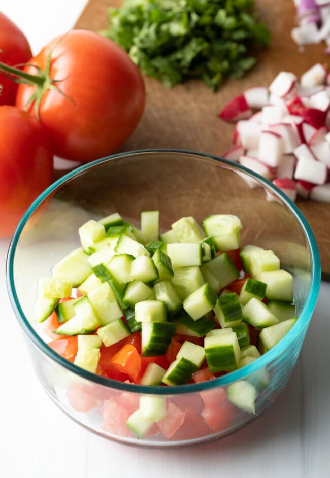 Chopped cucumber added to the glass bowl with tomatoes.