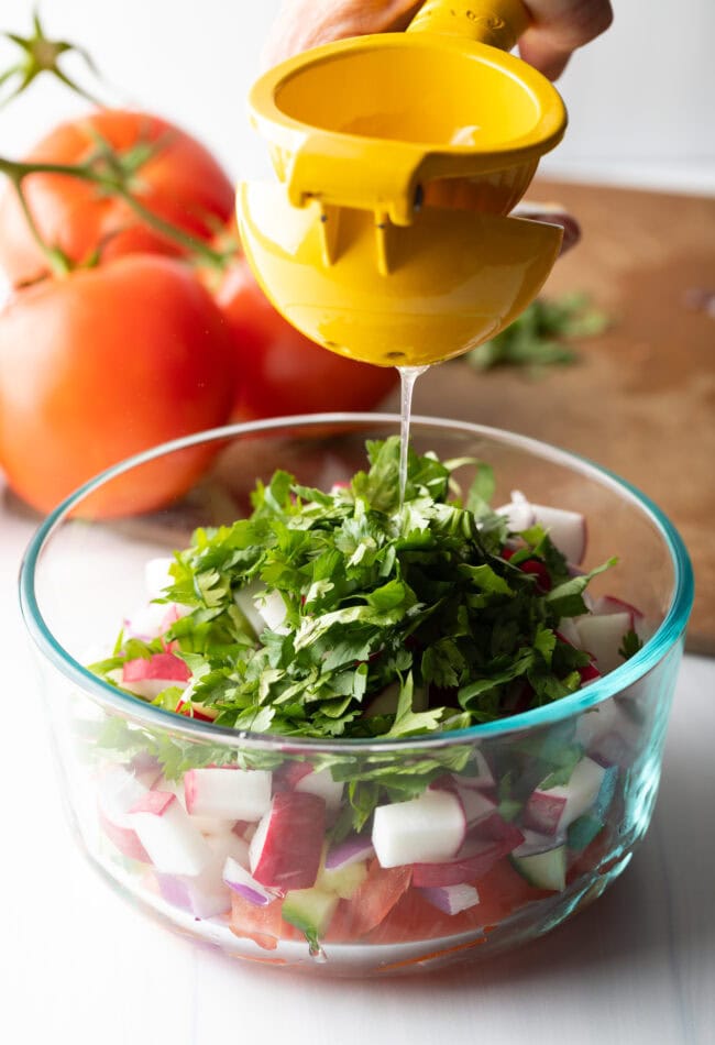 Adding freshly squeezed lemon juice to the bowl with veggies.