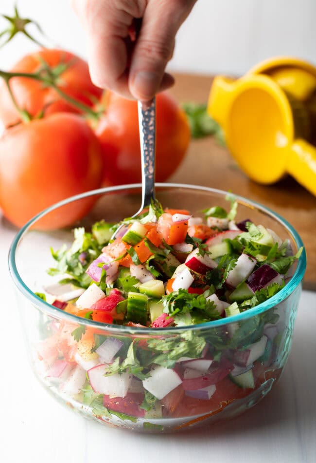 Chopped kachumber India salad in a glass bowl with a metal spoon.