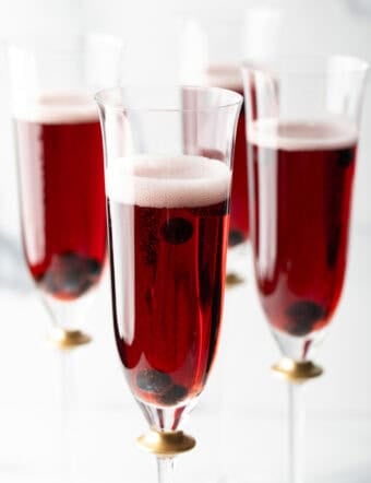 Four fluted glasses with deep red kir royale cocktail drinks.