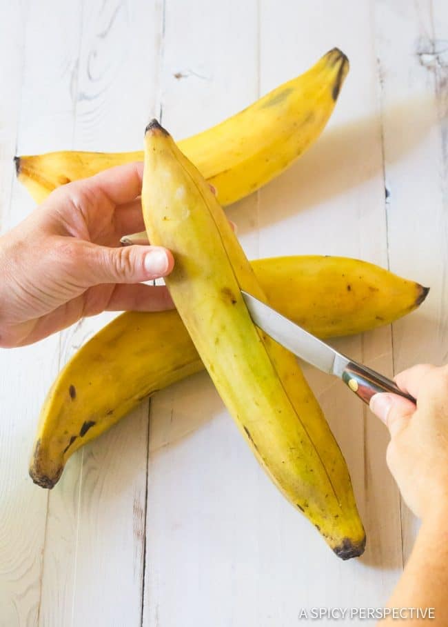 A hand scoring unripe plantains with a knife.
