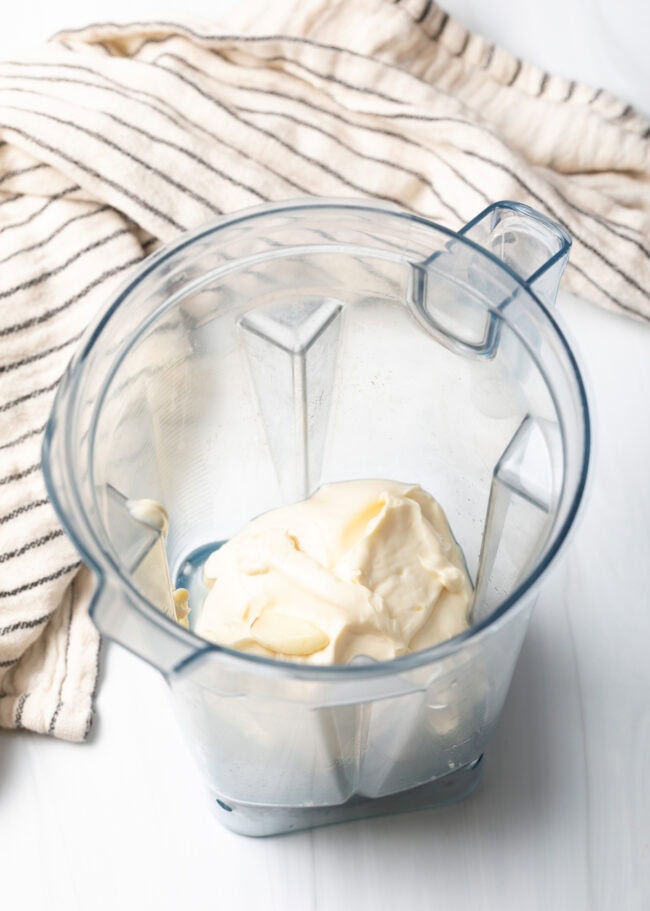 Open blender jar with mayo and garlic at the bottom.