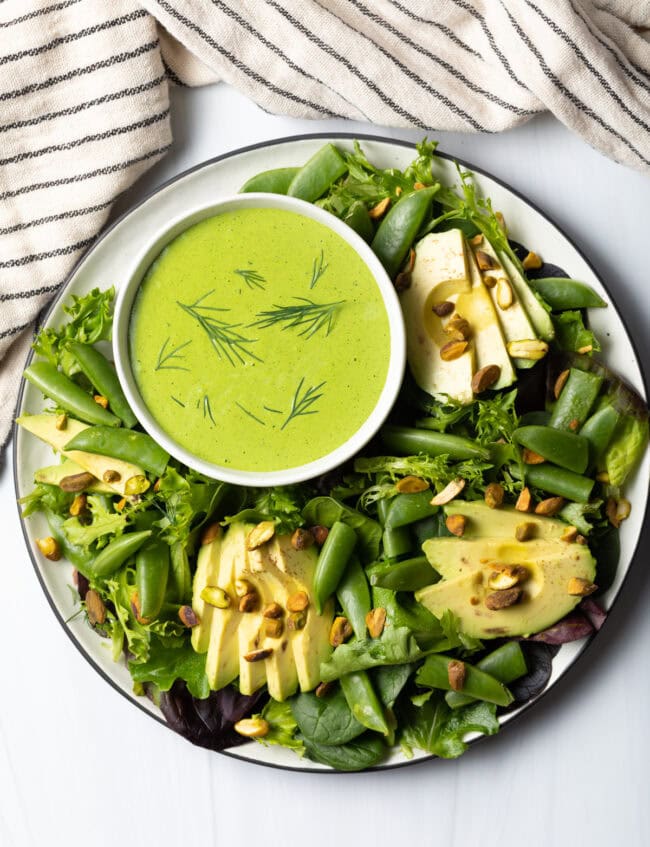 Top down view salad with bowl of vegan green goddess dressing.