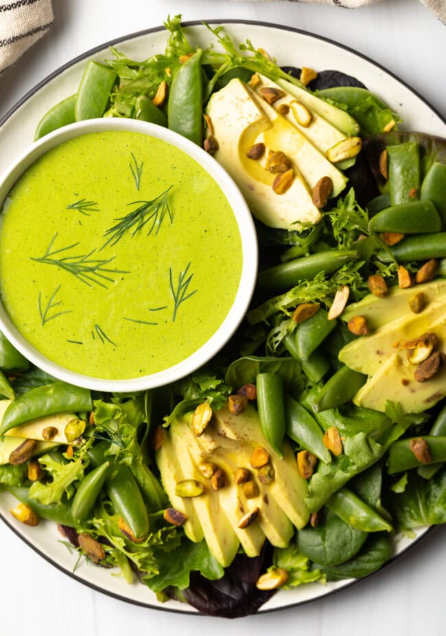 Top down view bowl of green salad with ramekin of dressing.