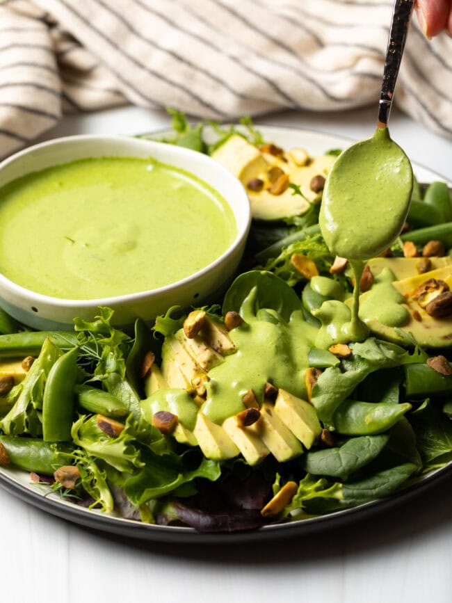 Spoon drizzling green goddess dressing onto a salad.