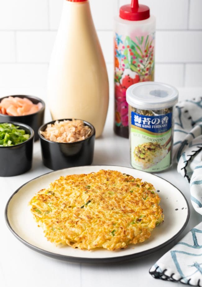 Japanese pancake on a plate with topping ingredients in the background