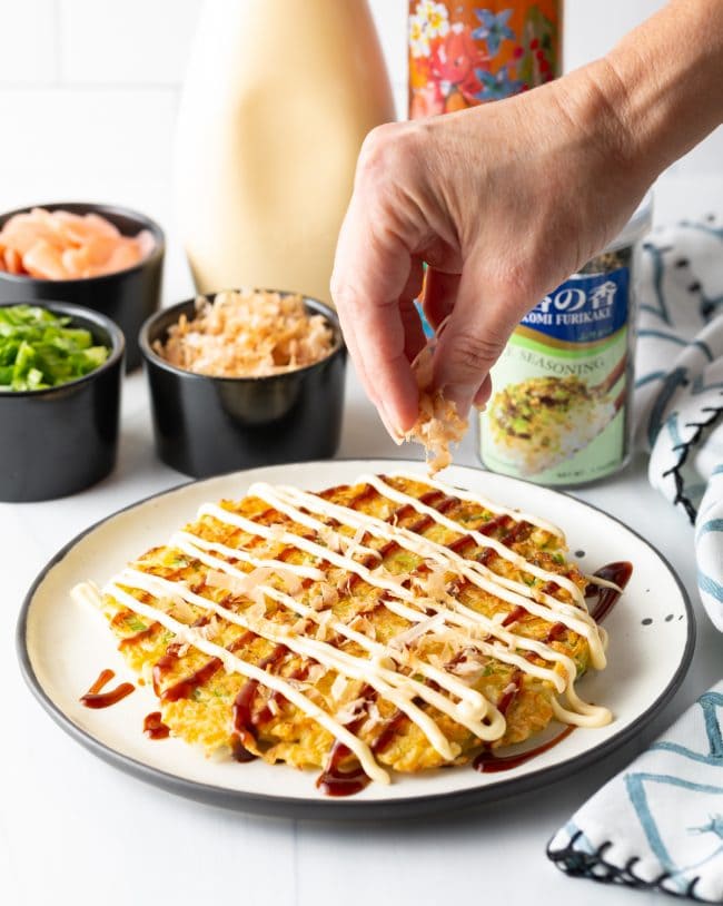 Hand sprinkling bonito flakes onto the okonomiyaki. 