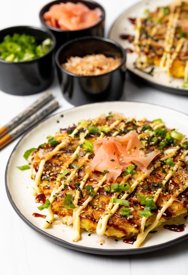 side view of finished Japanese cabbage pancake with loaded with scallions, ginger, kewpie mayo, and Okonomiyaki sauce