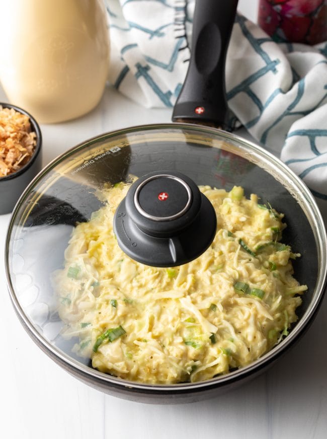 large skillet with uncooked pancake covered with a lid