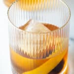 Old fashioned cocktail in a lowball glass, with single large cube of ice, cherry and orange peel in the glass.