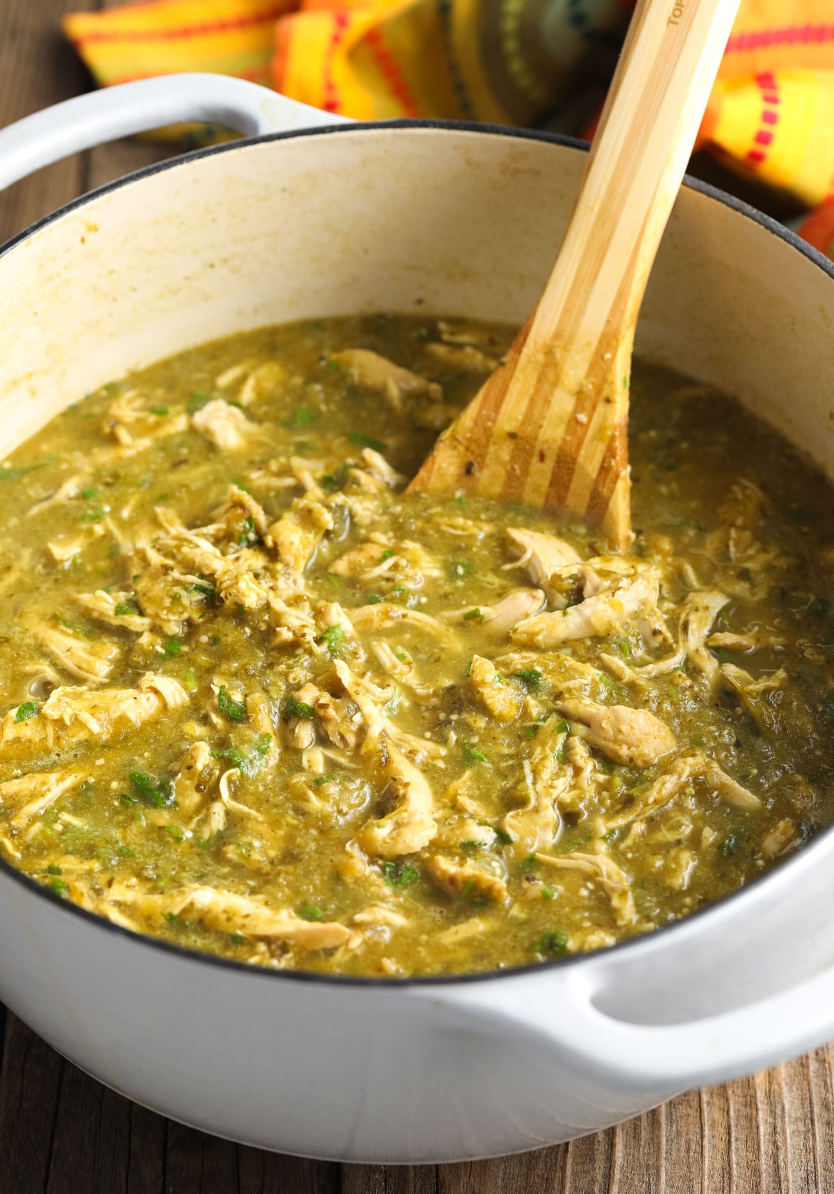 Side view of a wooden spoon stirring the final chicken chili soup in a pot 
