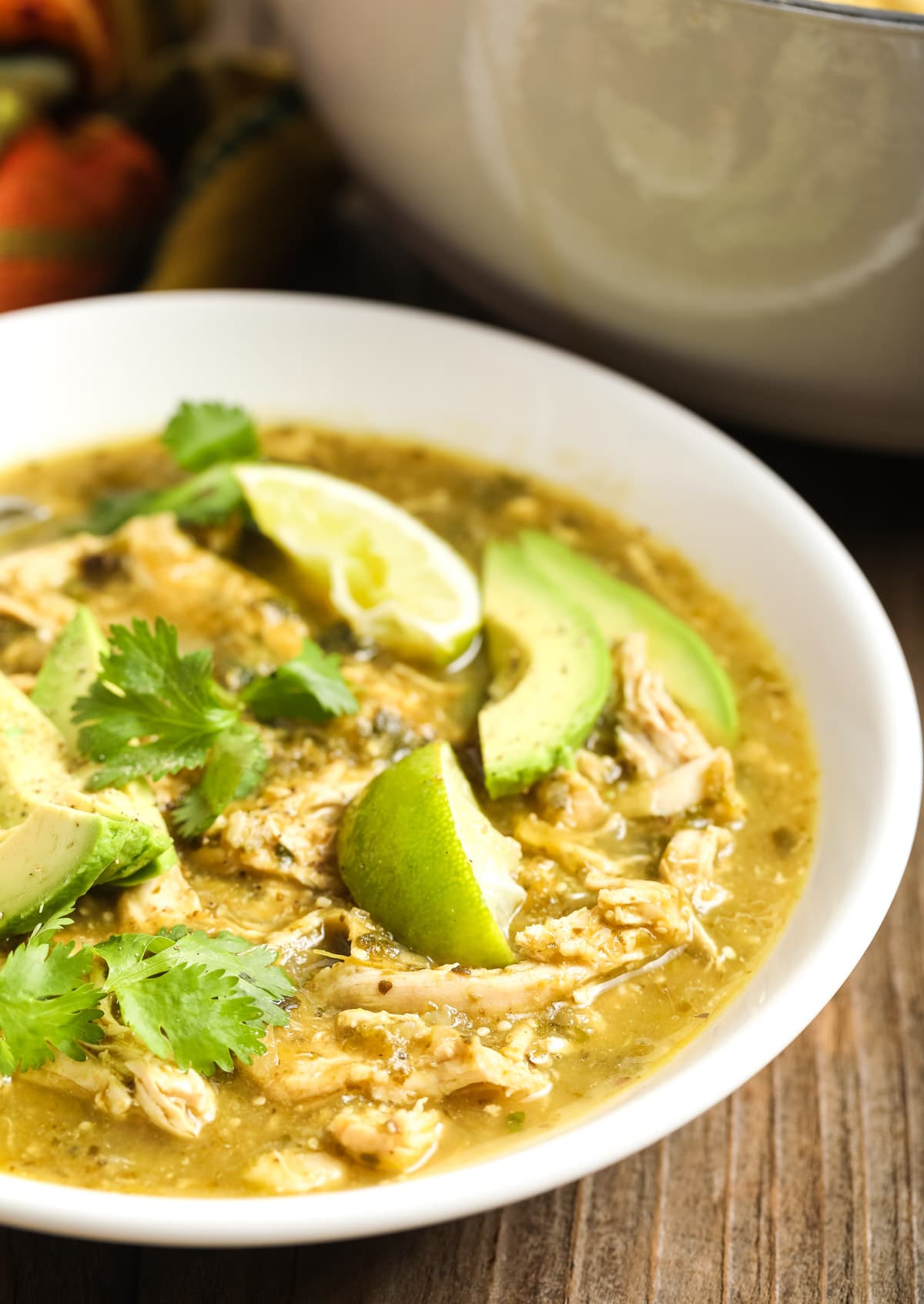 Side view of the chicken chili in a bowl topped with avocado and limes 
