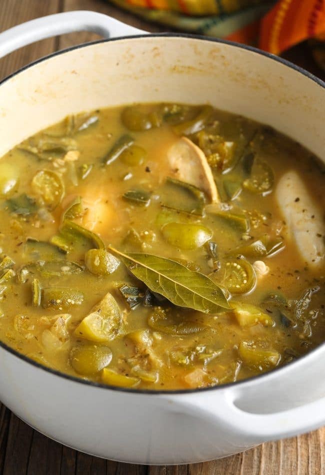 The chili cooking on the stove with a floating bay leaf and whole chicken 
