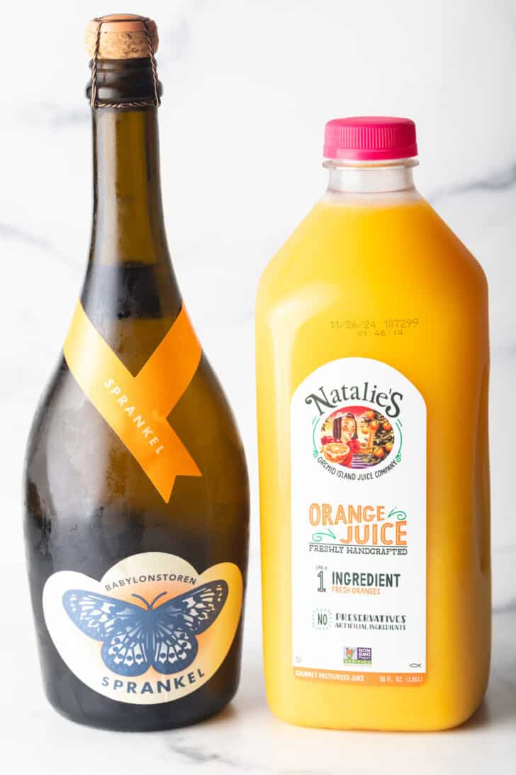 A bottle of champagne next to a bottle of orange juice.