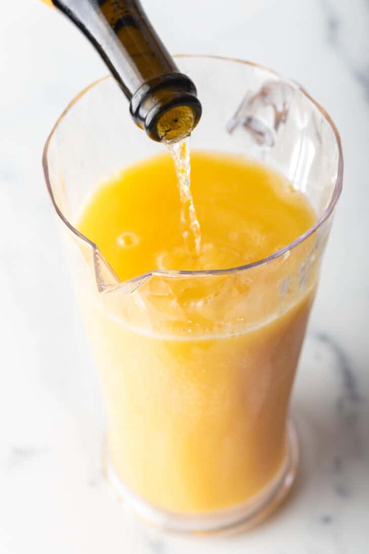 Pouring sparkling wine form the bottle into a glass pitcher with orange juice.