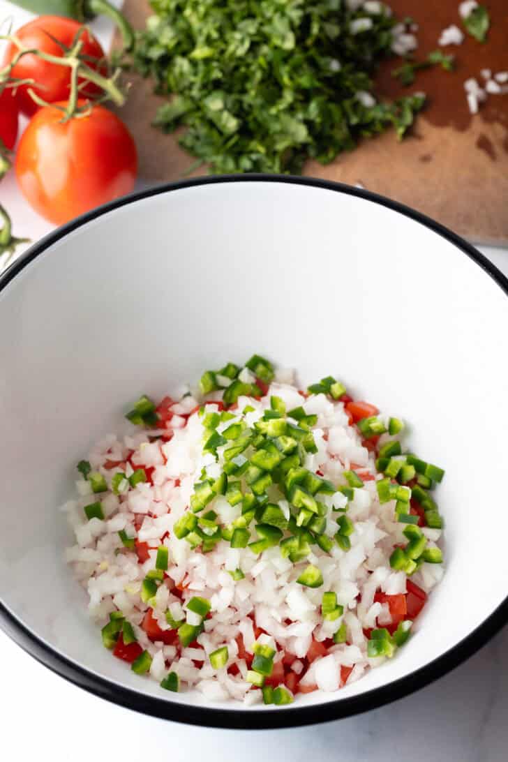 Chopped jalapenos and onion added to the bowl of chopped tomatoes.