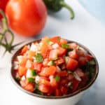 A white bowl of fresh pico de gallo with chopped tomatoes, onion, jalapeno, and cilantro.