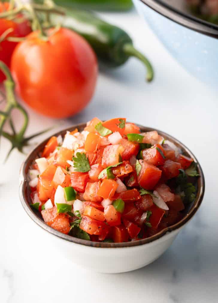 A white bowl of fresh pico de gallo with chopped tomatoes, onion, jalapeno, and cilantro.